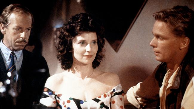 Judith Wiener in einem Kleid steht zwischen zwei Männern in einem Raum, links von ihr Dr. Alfons Schlögel