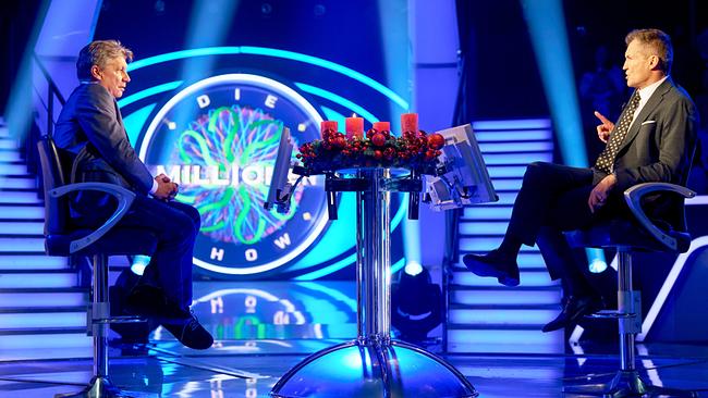 Hans Bürger und Armin Assinger sitzen sich in der Mitte des "Millionenshow"-Studios an einem Tisch mit Adventskranz gegenüber und unterhalten sich.