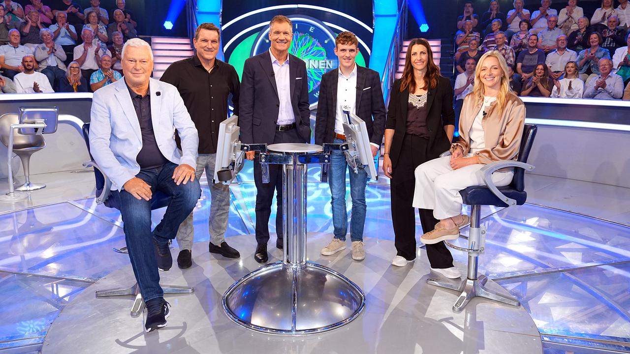 © ORF/Stefan Gregorowius Toni Polster, Andreas Herzog, Armin Assinger, Johannes Aigner, Janine Flock und Lisa Hauser posieren im "Millionenshow"-Studio vor einem applaudiernden Publikum.