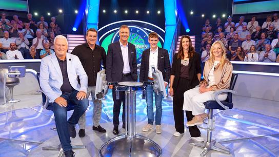 Toni Polster, Andreas Herzog, Armin Assinger, Johannes Aigner, Janine Flock und Lisa Hauser posieren im "Millionenshow"-Studio vor einem applaudiernden Publikum.