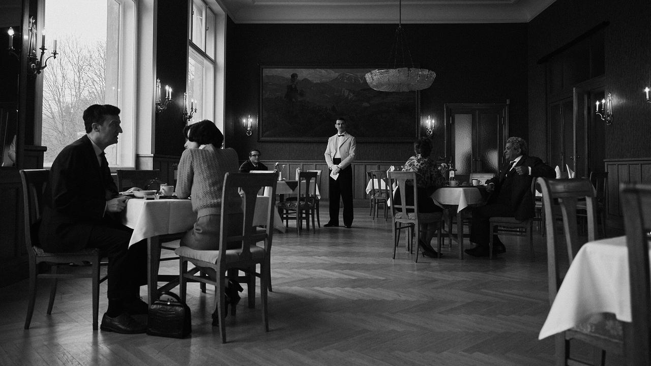 Der Frühstückssaal des Hotels, in dem Gäste an kleinen Tischen sitzen in einem eleganten, historischen Speisesaal, während ein Kellner in der Mitte steht.