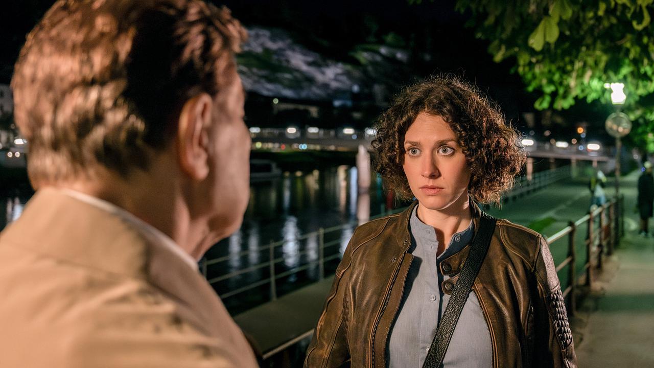 Alfons Seywald und Irene Russmeyer führen nachts ein Gespräch an einer Uferpromenade.