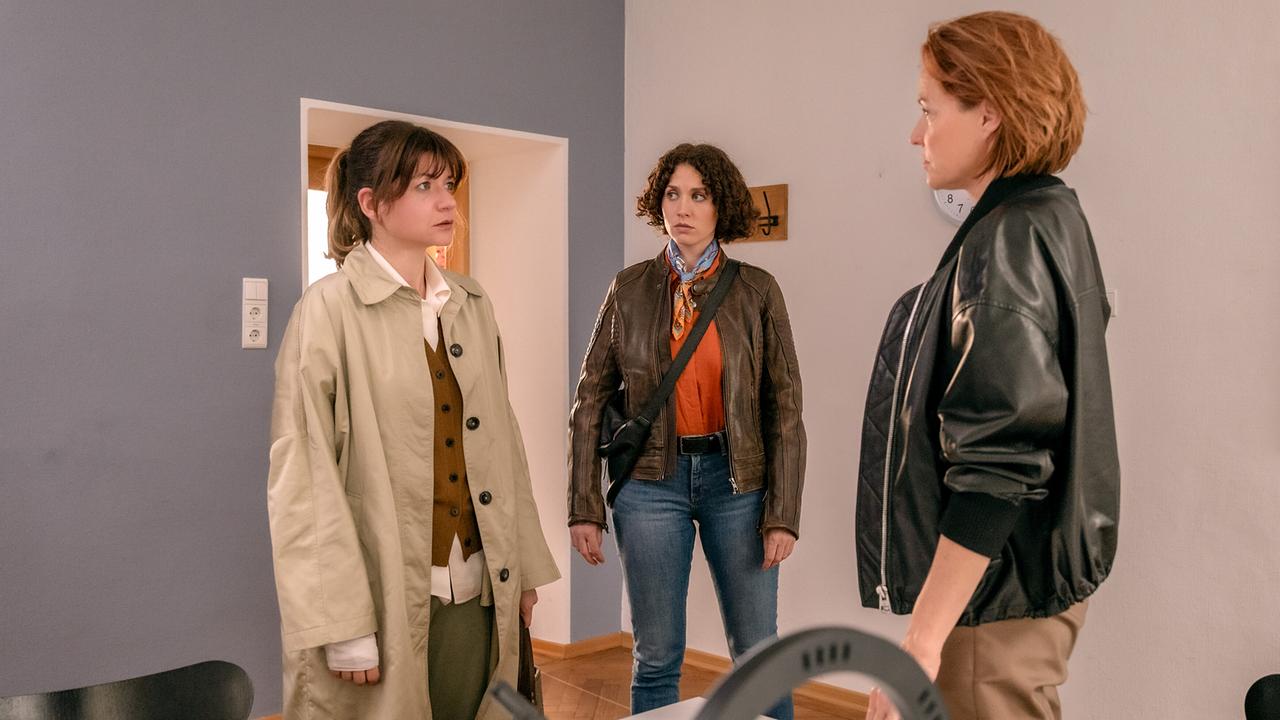 Eva Lackner, Irene Russmeyer und Lu Frey stehen in einem schlichten Raum und sprechen miteinander.