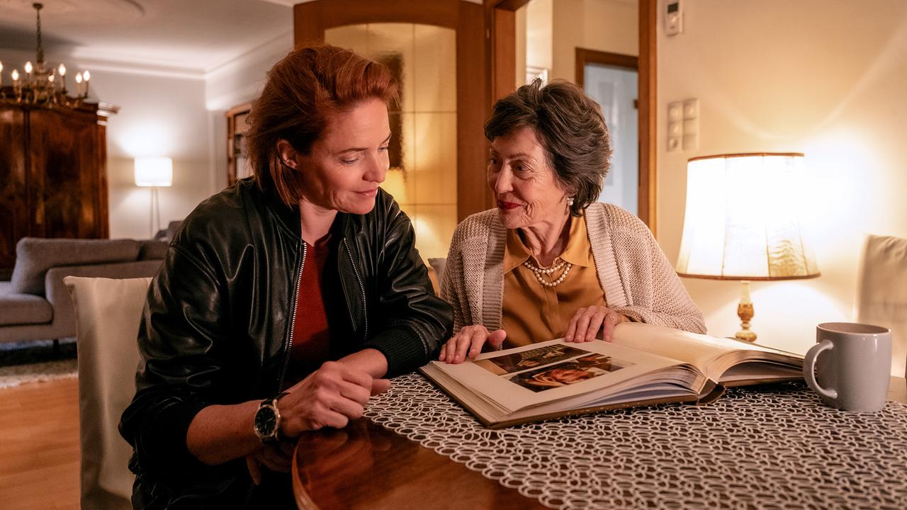 Lu und Klara Frey sitzen gemeinsam an einem Wohnzimmertisch und blättern in einem Fotoalbum