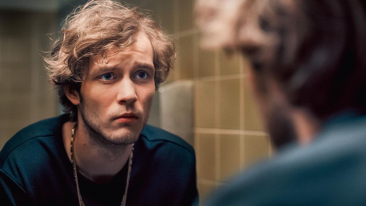 © ORF/Graf Film/Lukas Gnaiger Tassilo Kurka sieht sich nachdenklich im Spiegel eines gekachelten Waschraums an.