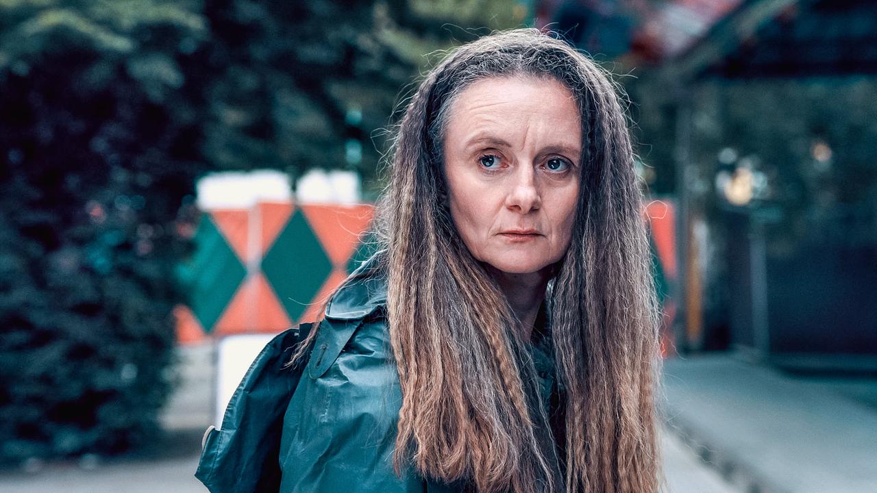 © ORF/Graf Film/Lukas Gnaiger Peggy Renoldi steht im Freien vor bunten Jahrmarktdekor‑Elementen