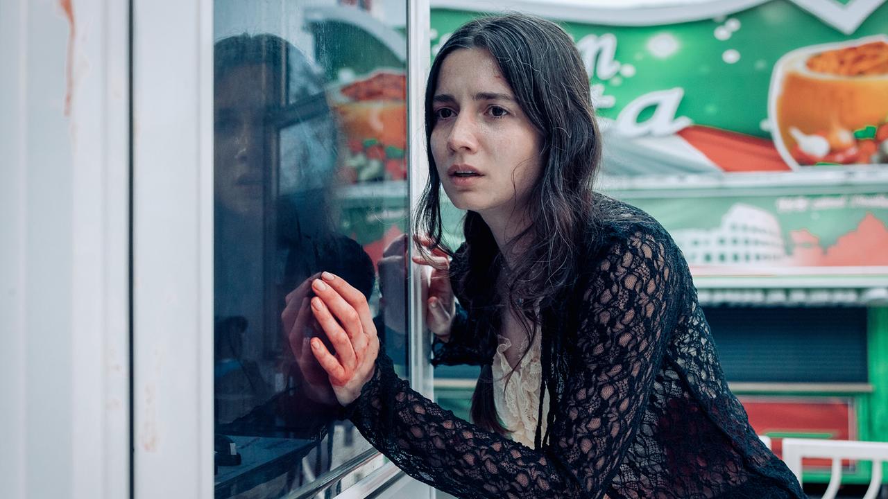 © ORF/Graf Film/Manuel Riesterer Lorena Meloyan lehnt an einem Fenster einer Jahrmarktsbude und blickt ernst.