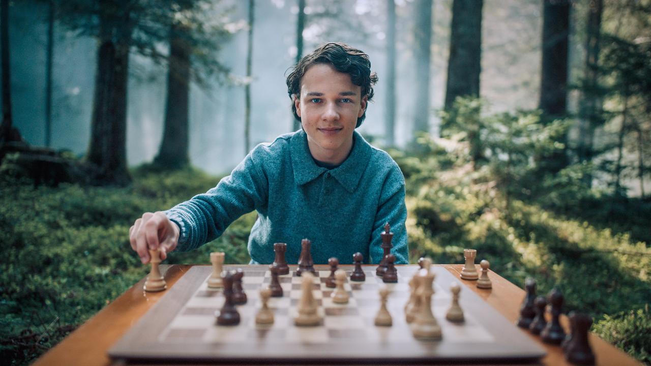 © ORF/Graf Film/Lukas Gnaiger Lukas Hanauer sitzt mitten in einem sonnigen Wald an einem Tisch und spielt Schach.