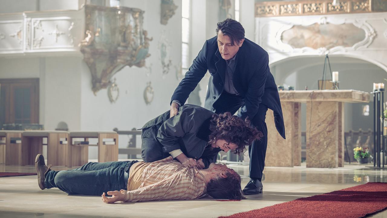 © ORF/Graf Film/Manuel Riesterer In einer Kirche beugt sich Mara Eisler über den blutenden Jasper Bell, der am Boden liegt. Thomas Komlatschek versucht Mara Eisler zurückzuhalten.