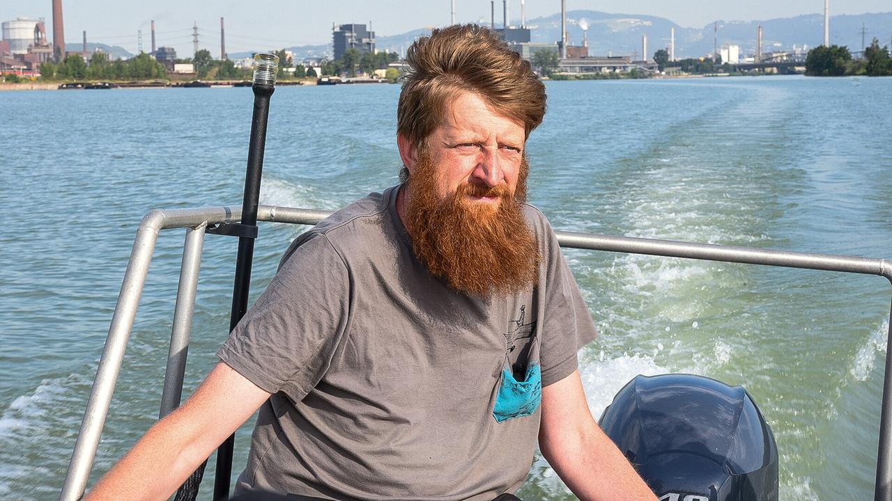© ORF/Produktion West/Gerhard Mader Franz Wiesmayr sitzt auf einem Boot auf der Donau vor Industriekulisse.