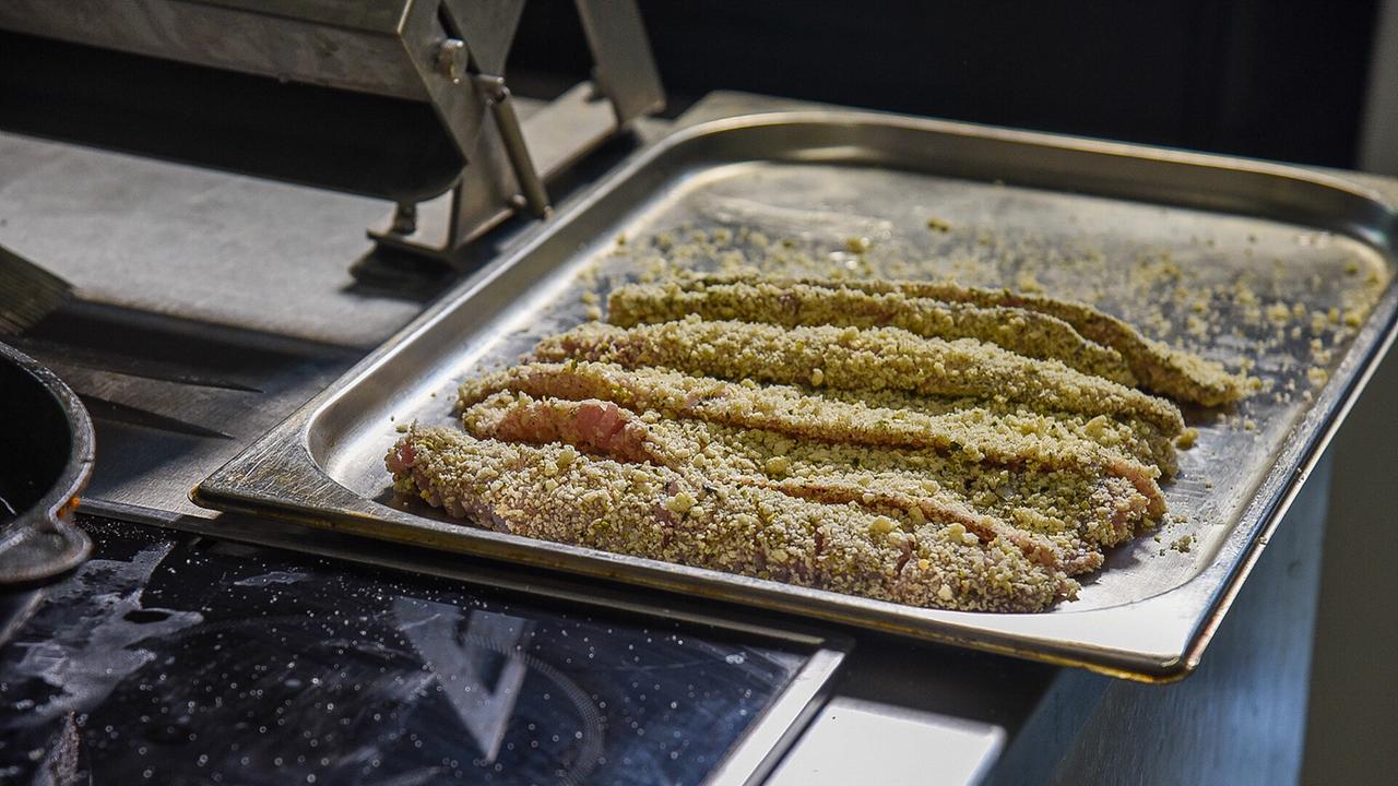 © ORF/Produktion West/Gerhard Mader Frische Fischfilets in Panade auf einem Backblech neben einem Herd.