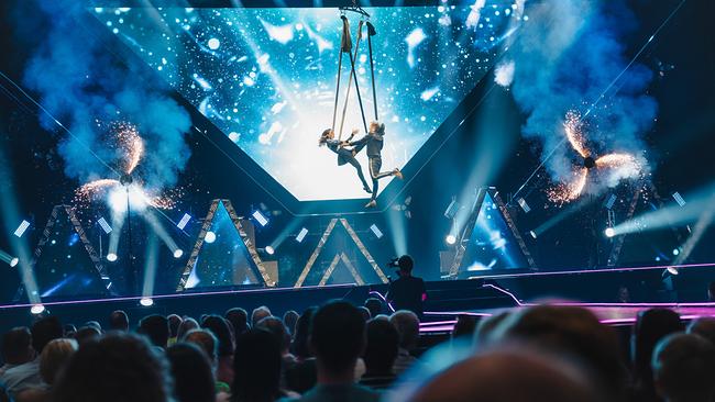 Amélie van Tass und Thommy Ten schweben bei einer spektakulären Luftakrobatik‑Nummer vor einer leuchtenden Bühnenkulisse.