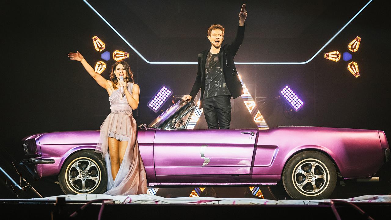 Amélie van Tass und Thommy Ten stehen neben einem violetten Cabrio und präsentieren sich vor einer beleuchteten Kulisse.