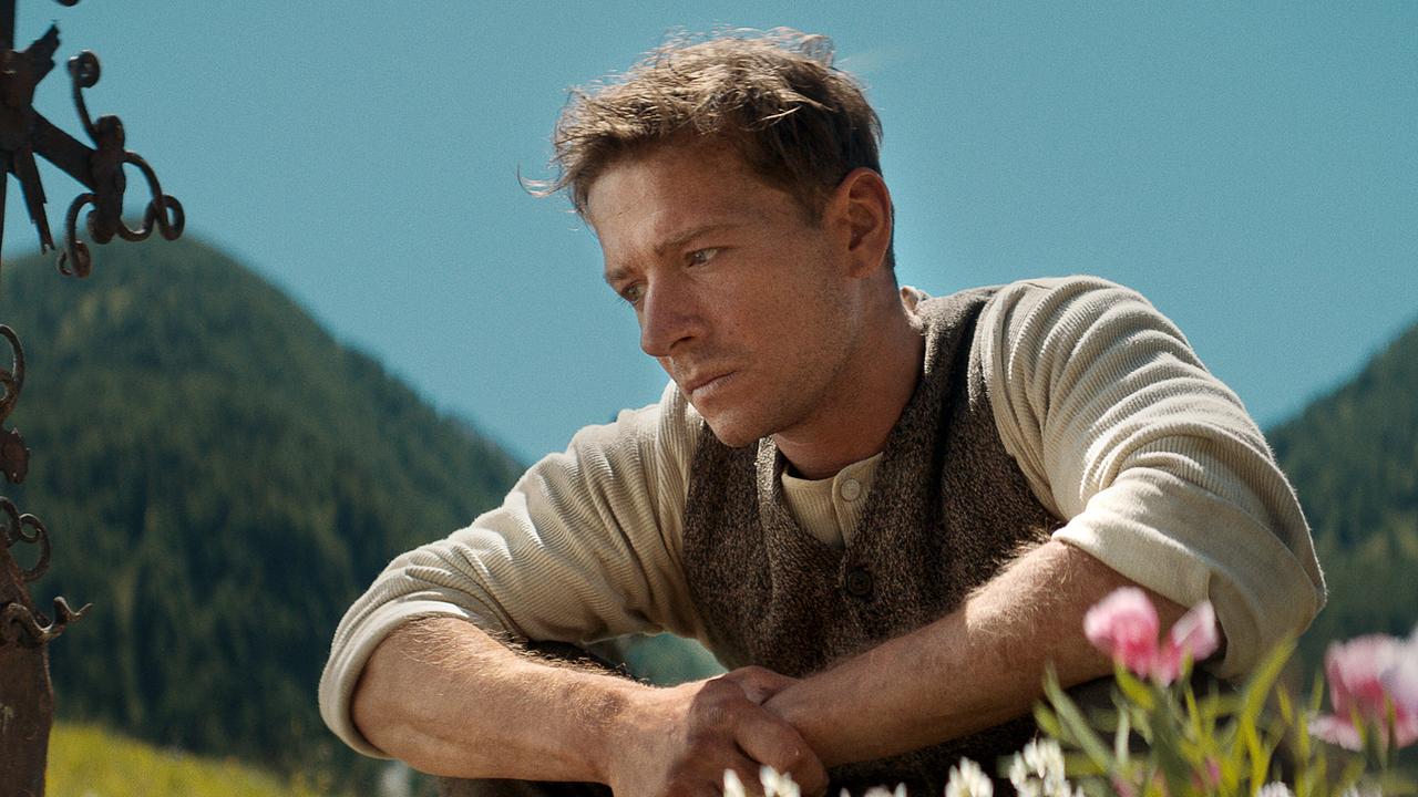 Der junge Andreas Egger hockt auf einer blühenden Almwiese und schaut nachdenklich.