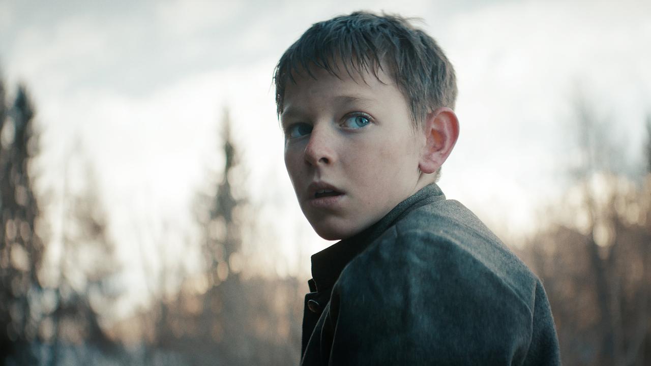 Andreas Egger als Kind steht im Freien und dreht sich leicht zur Seite, während Bäume im Hintergrund zu sehen sind.