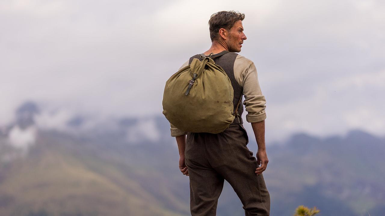 Der junge Andreas Egger trägt einen großen Rucksack und blickt über die weiten Berge.