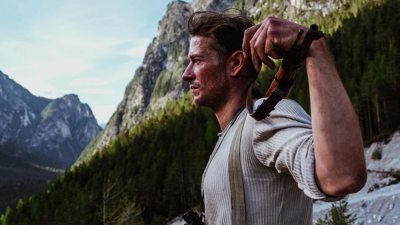 Der junge Andreas Egger mit Wanderwerkzeug über der Schulter steht in einer felsigen Berglandschaft.