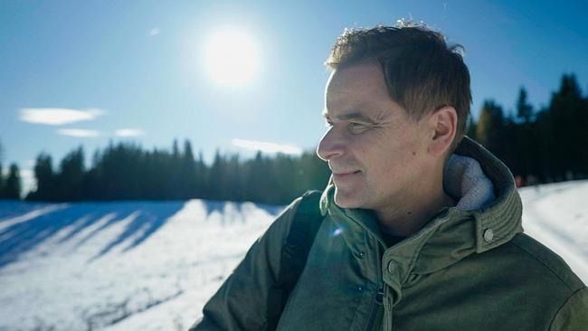 © ORF/Good Media Solutions Edgar Unterkirchner im Anorak blickt in die Ferne in einer sonnigen Winterlandschaft mit Schnee und Wald im Hintergrund.