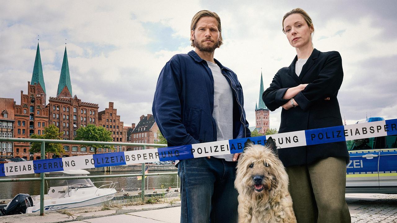 © ORF/RTL/Sandra Hoever Eric Seeler und Kommissarin Hannah Vogt stehen hinter einem Absperrband der Polizei und blicken Richtung Kamera.