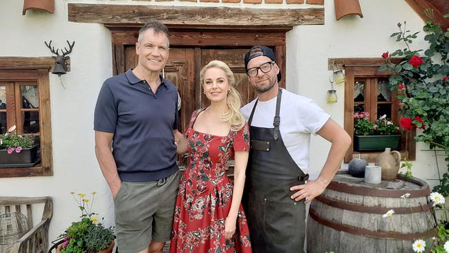 Armin Assinger, Silvia Schneider und Robert Buchberger posieren vor dem Eingang eines rustikalen Hauses.
