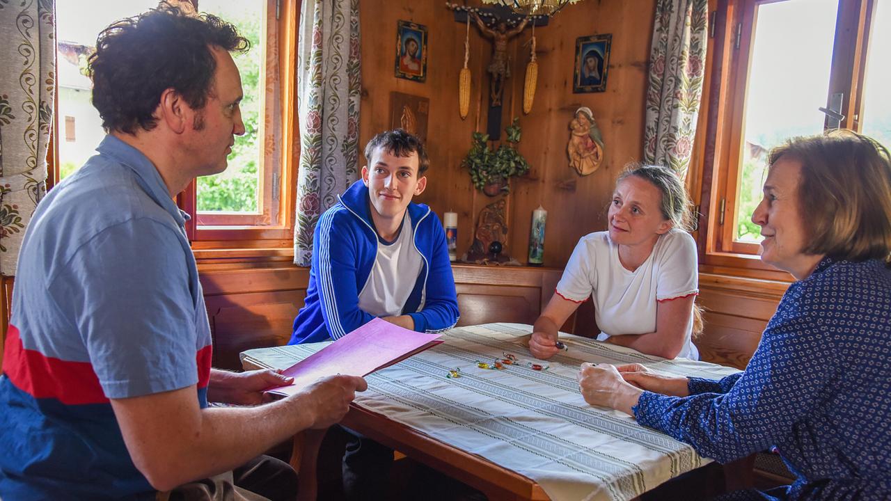 Sepp sitzt mit seiner Schwester Gertrude, seinem jüngerer Bruder Jakob und seiner Mutter Johanna  in einer holzvertäfelten Stube gemeinsam an einem Tisch und informiert die Familie über seine Pläne. 