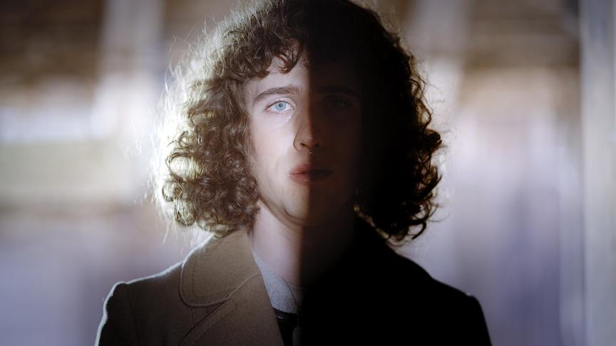 © ORF/Lotus Film/Zeitsprung Pictures Erika steht mit lockigem langen Haar in einem Innenraum, halb im Licht und halb im Schatten.