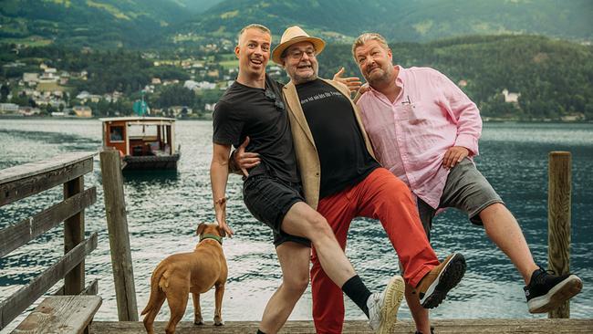 Matthias Franz Stein, Erwin Steinhauer und Achim Schneyder albern mit einem Hund auf einem Steg vor einer alpinen Seelandschaft herum.