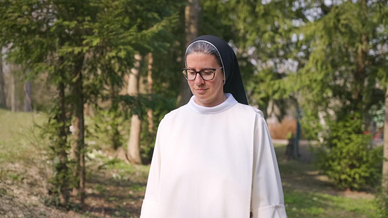 Sr. Franziska Madl im weißen Ordenskleid und schwarzem Schleier im Freien zwischen Bäumen.