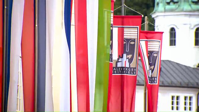 © ORF Bunte Fahnen und rote Banner der Salzburger Festspiele hängen entlang einer Straße.