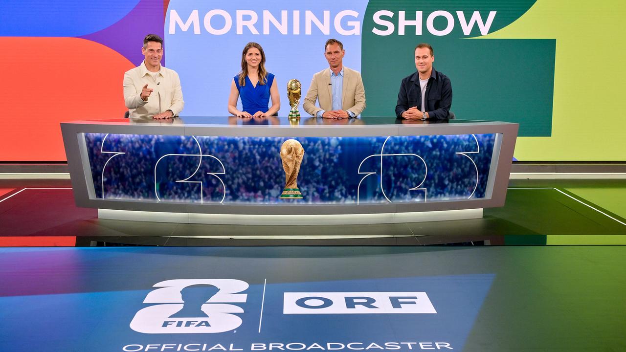 Helge Payer, Kristina Inhof, Christian Diendorfer und Michael Liendl sitzen hinter einem großen Studiotisch in einer farbenfrohen „Morning Show“-Kulisse, mit einer goldenen Fußball‑Trophäe im Zentrum und ORF‑/FIFA‑Branding im Vordergrund.