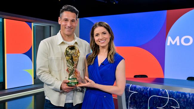 © ORF/Thomas Ramstorfer Helge Payer und Kristina Inhof stehen in einem modernen „Morning Show“-TV‑Studio und halten gemeinsam den goldenen Fußball‑WM-Pokal, während im Hintergrund der Studiotisch und die bunte Kulisse zu sehen sind.