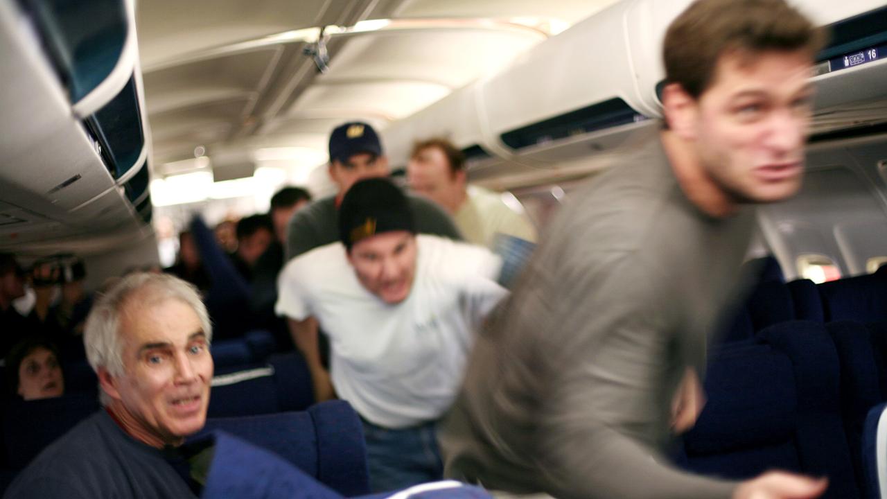 Männer laufen durch die Sitzreihen eines Passagierflugzeugs nach vorne Richtung Cockpit