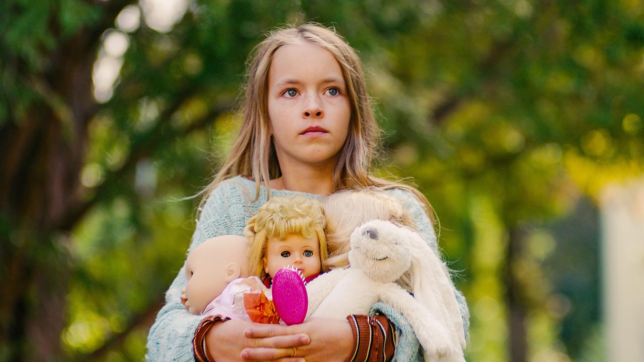 © ORF/Film AG Gina hält im Grünen mehrere Puppen und ein Stofftier fest an sich gedrückt.