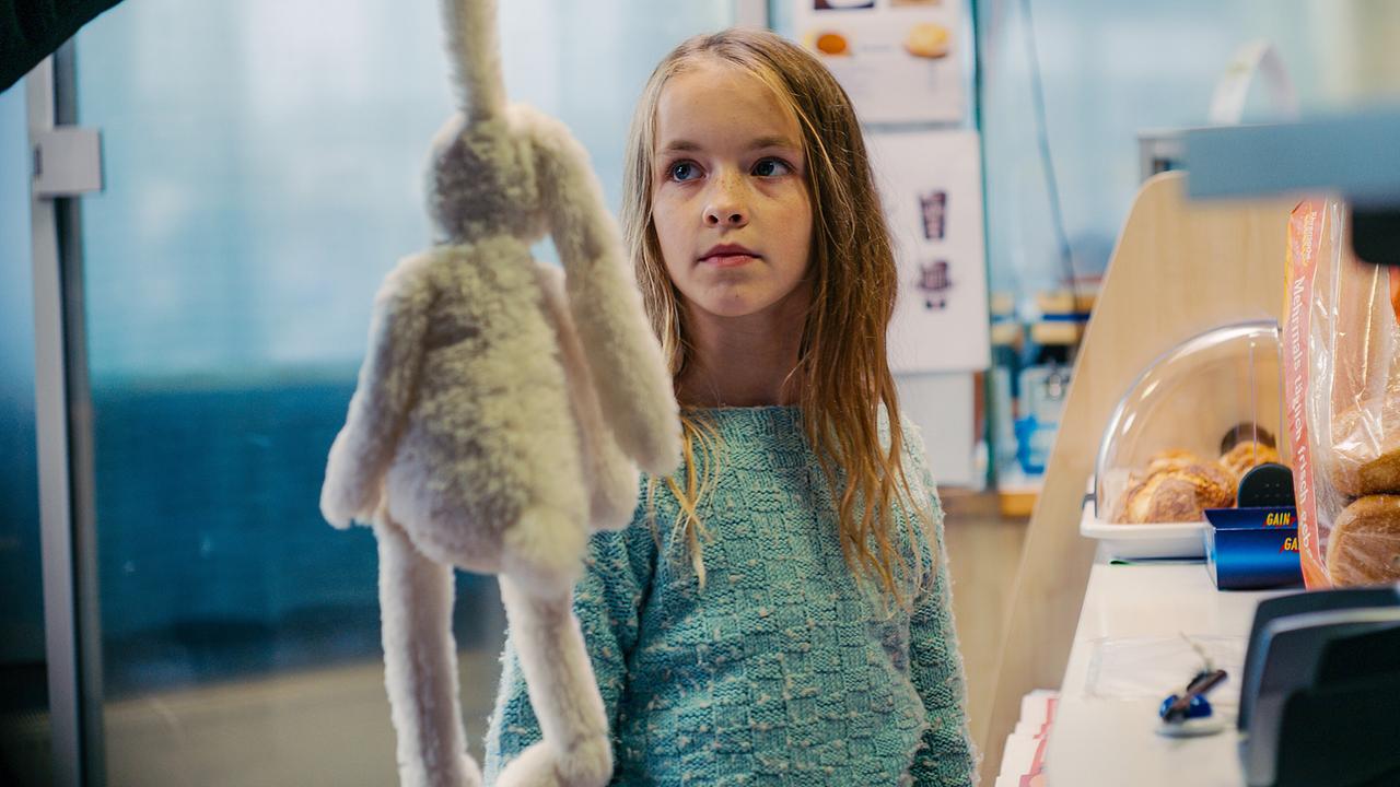 © ORF/Film AG Jemand hält vor Gina einen Stoffhasen an der Kasse eines Geschäfts.