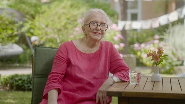 © ORF/FFP Filmproduktion Esther Vilar mit großer Brille und pinker Bluse sitzt an einem Gartentisch neben einer kleinen Blumenvase.