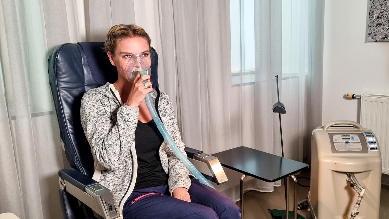 © ORF/Kiwi TV Christine Reiler beim Höhentest sitzt bei einer medizinischen Anwendung mit Atemmaske in einem Behandlungsraum.