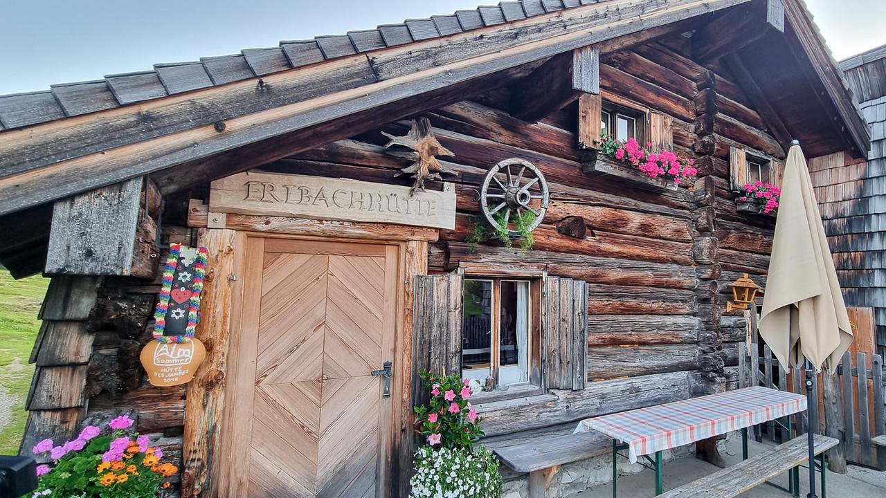 © ORF/Kiwi TV Die Erlbachhütte, eine urige Almhütte, mit Blumen an den Fenstern und Holzbänken