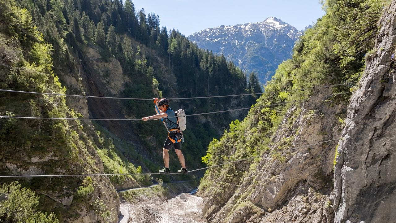 © ORF/Kiwi TV Ein gesicherter Mann balanciert auf einer Highline über einer tiefen Gebirgsschlucht am Klettersteig Simmswasserfall.