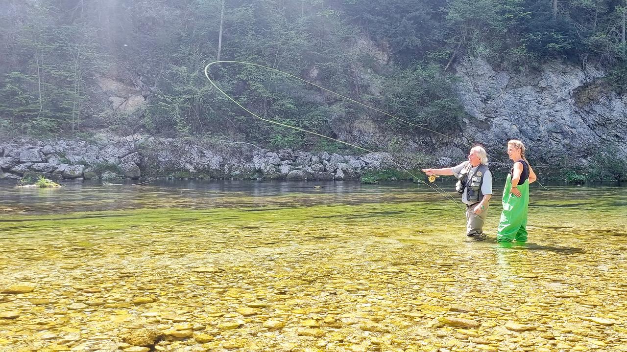 © ORF/Kiwi TV Franz Rosenberger und Christine Reiler stehen beim Fliegenfischen in einem sonnigen Flusslauf.
