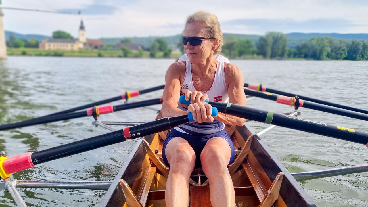 © ORF/Kiwi TV Drei Ruderinnen und Ruderer vom Steiner Ruderclub rudern konzentriert in einem schmalen Boot auf einem ruhigen Fluss.
