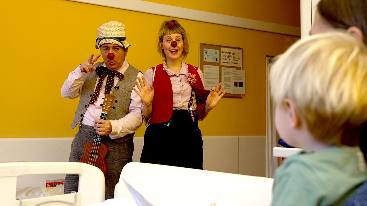 Zwei Rote Nasen Clowns unterhalten ein Kind im Krankenhauszimmer