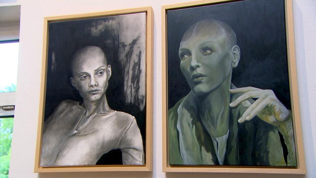 Zwei großformatige Porträts einer Frau ohne Haare, gemalt von Ulrike Eidenberger, hängen nebeneinander an einer Wand in einem Innenraum.