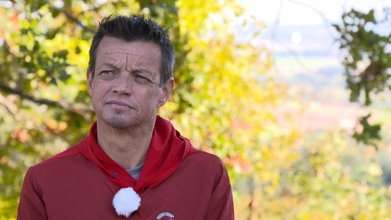 Helmut Steigersdorfer mit einer Spenderlunge steht im Freien vor herbstlich gefärbten Bäumen und trägt sportliche Kleidung mit einem Mikrofon.