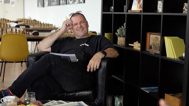 Andres Frank sitzt in einem Coachsessel neben einem Regal, dahinter Tische, auf denen Schachbretter liegen.