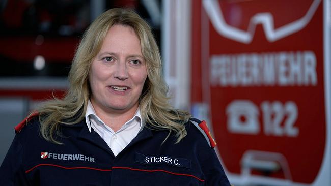 Feuerwehrfrau Claudia Sticker vor Grafik der Freiwilligen Feuerwehr