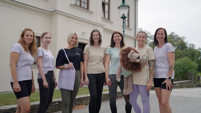 © ORF/MC Digitalproduktions GmbH Team Löwenmut, eine Gruppe von sieben Frauen, steht mit einer Löwen-Handpuppe vor einem Gebäude.