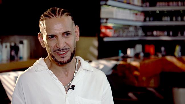 © ORF/MC Digitalproduktions GmbH Yochai Mevorach, Frisör und Gründer des Vereins „Haarfee“, mit geflochtenem Haar und Ansteckmikrofon spricht in einem Friseurstudio in die Kamera.