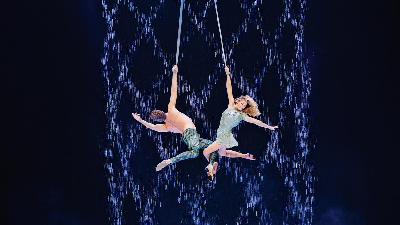 © ORF/MDR/Universal Music/Sandra Lude Helene Fischer schwingt mit einem weiteren Artisten an Seilen vor einem dunkelblauen, wasserfallartigen Bühnenhintergrund durch die Luft.
