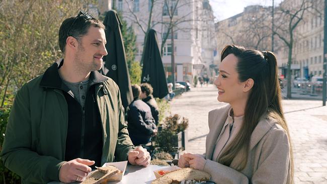 Ferdinand Seebacher und Sasa Schwarzjirg stehen an einem Stehtisch im Freien, essen belegte Brote und unterhalten sich in einer städtischen Umgebung.