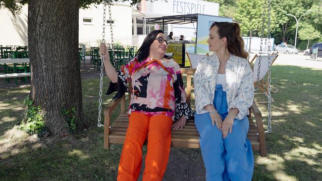 © ORF/TVfriends Maria Happel und Sasa Schwarzjirg unterhalten sich auf einer Holzschaukel im Schatten eines Baumes vor dem Festspielgelände.